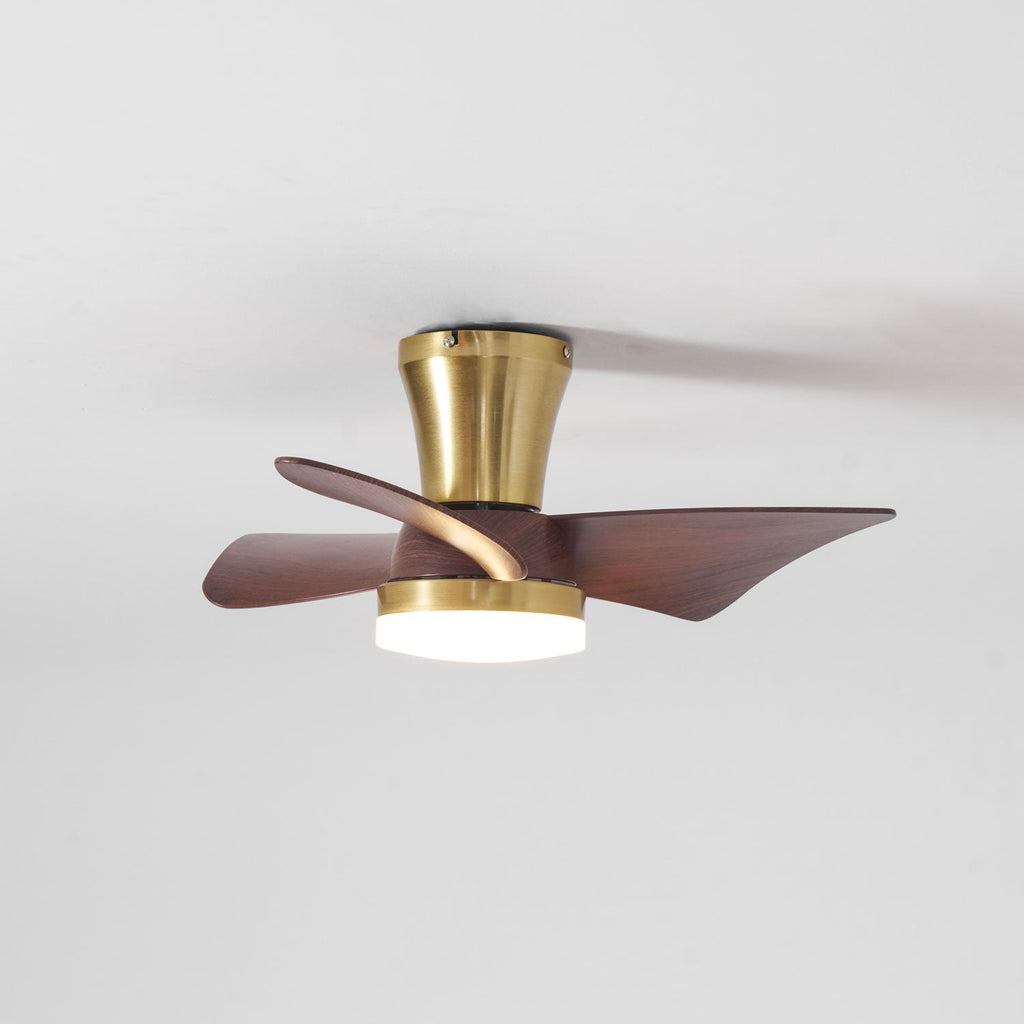 A Clérachic gold ceiling fan with its light on, the blades seen slightly blurred as they turn against a pale ceiling.