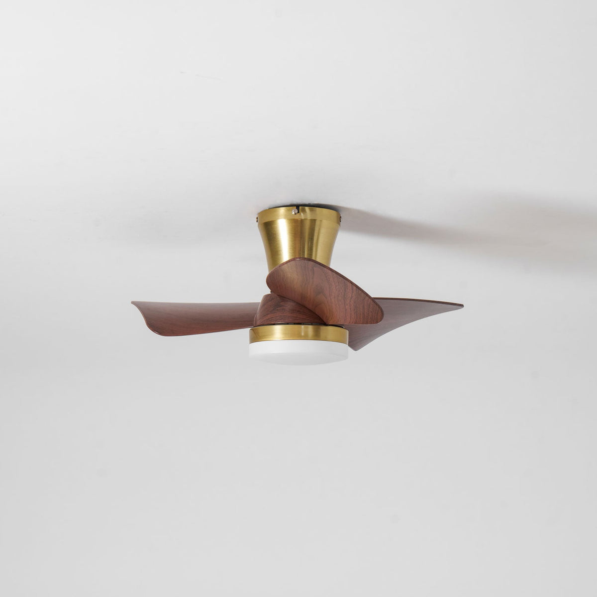 A side view of the Clérachic gold ceiling fan with an unlit white diffuser, blades slightly blurred against a grey-white ceiling.