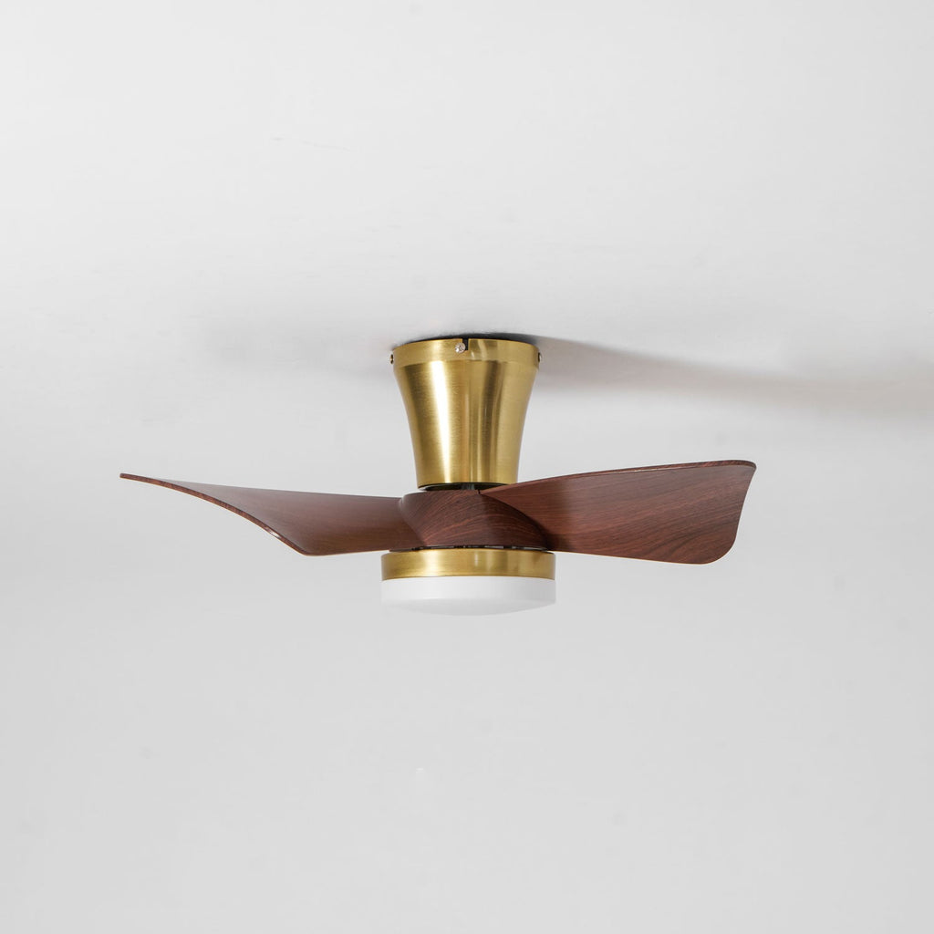 A low-angle view of the Clérachic gold ceiling fan, with its trumpet canopy, gold trim ring and unlit light under walnut-grain blades.