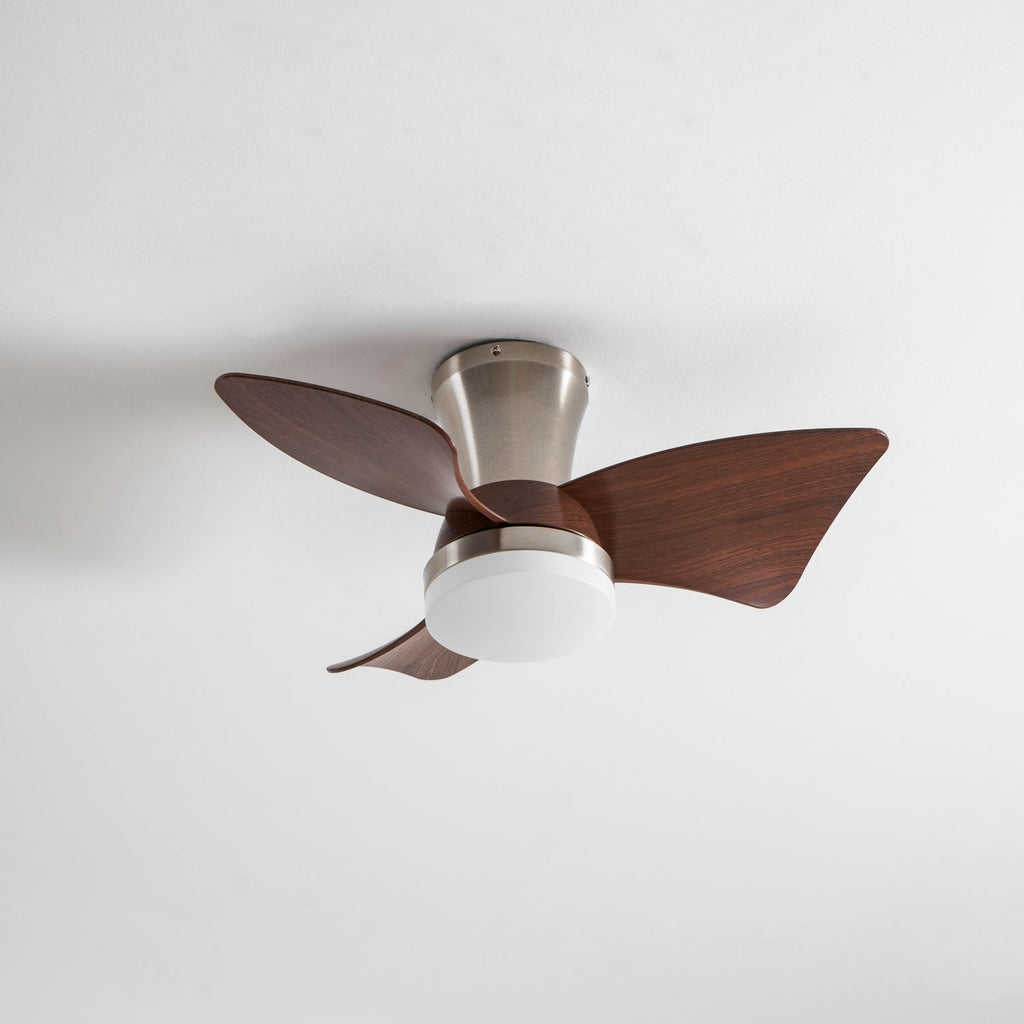 A nickel Clérachic ceiling fan with its light off, three walnut-grain blades and a white diffuser against a soft grey ceiling.
