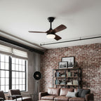 This Clérachic ceiling fan hangs in a loft living room with a red brick wall, black window frames and a leather sofa below.