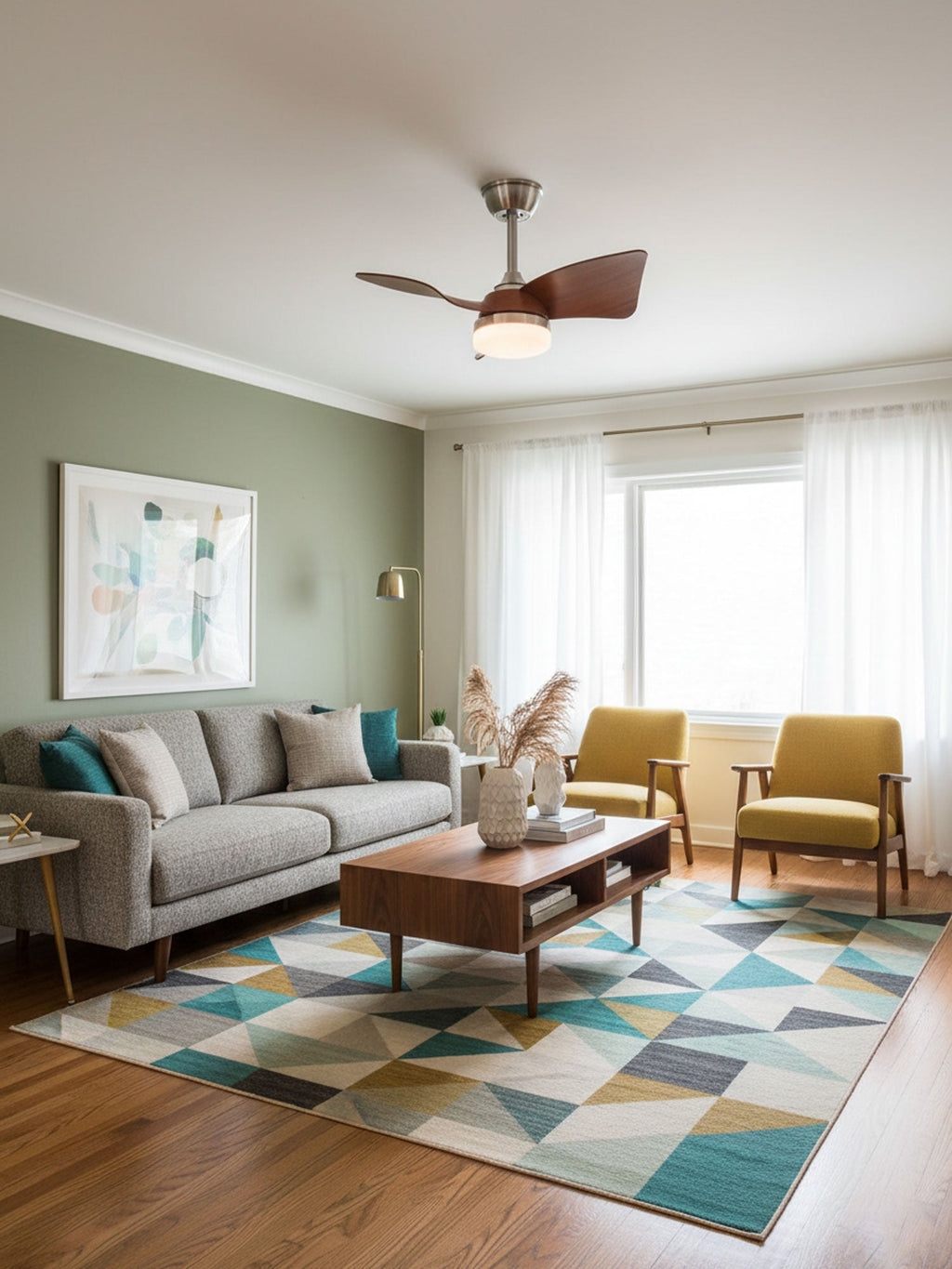 Walnut-tone fan blades and a lit white light under the ceiling of a sage-green living room with a geometric rug, from Clérachic.