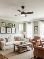 This Clérachic fan, with a black canopy and dark walnut blades, hangs in a bright living room with cream sofas and a jute rug.