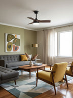 A compact Clérachic ceiling fan with slim walnut blades sits above a grey sofa and mustard armchair on a geometric rug.