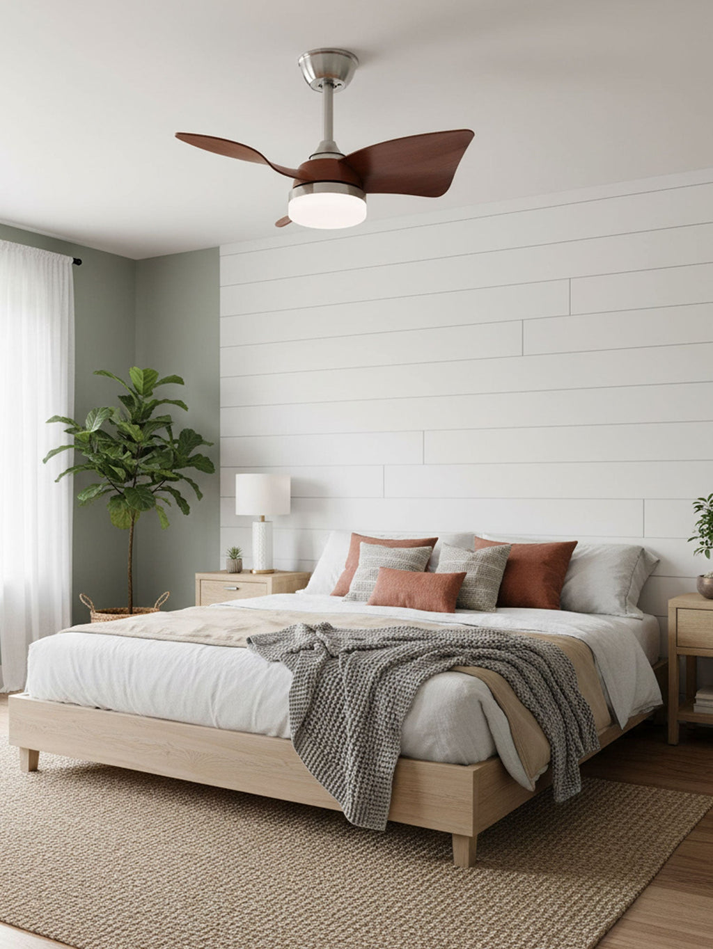 Short walnut blades and a lit white light on a Clérachic fan, above a bed with a grey throw against a white panelled wall.
