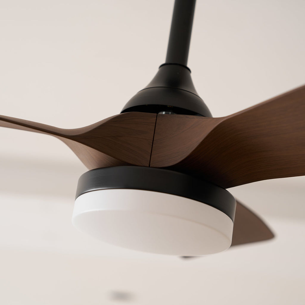 Close view of the white light cover and black ring beneath the walnut-grain blades on this Clérachic ceiling fan.