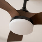 Close view of the round white light cover, black trim and the joint between two walnut-grain blades on this Clérachic fan.