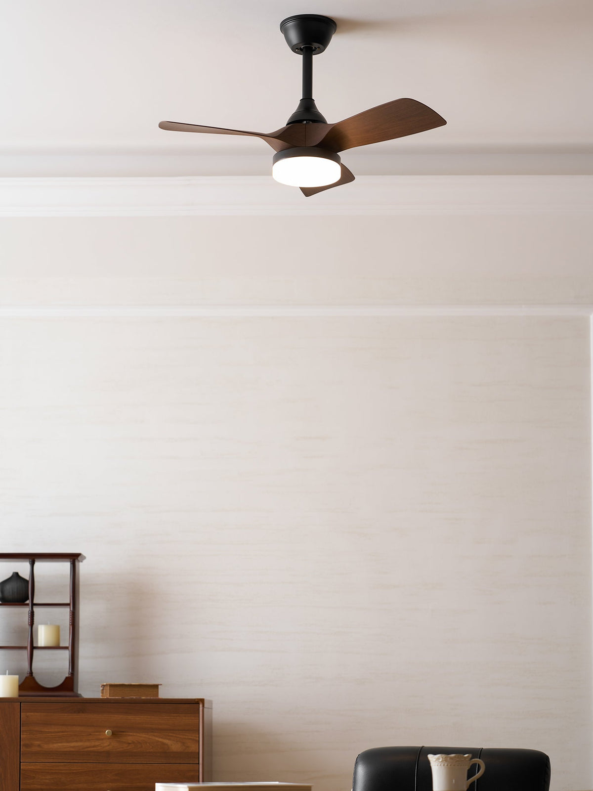 A Clérachic fan with walnut blades and a lit light, seen from a slightly different angle in a cream room with a wooden sideboard.