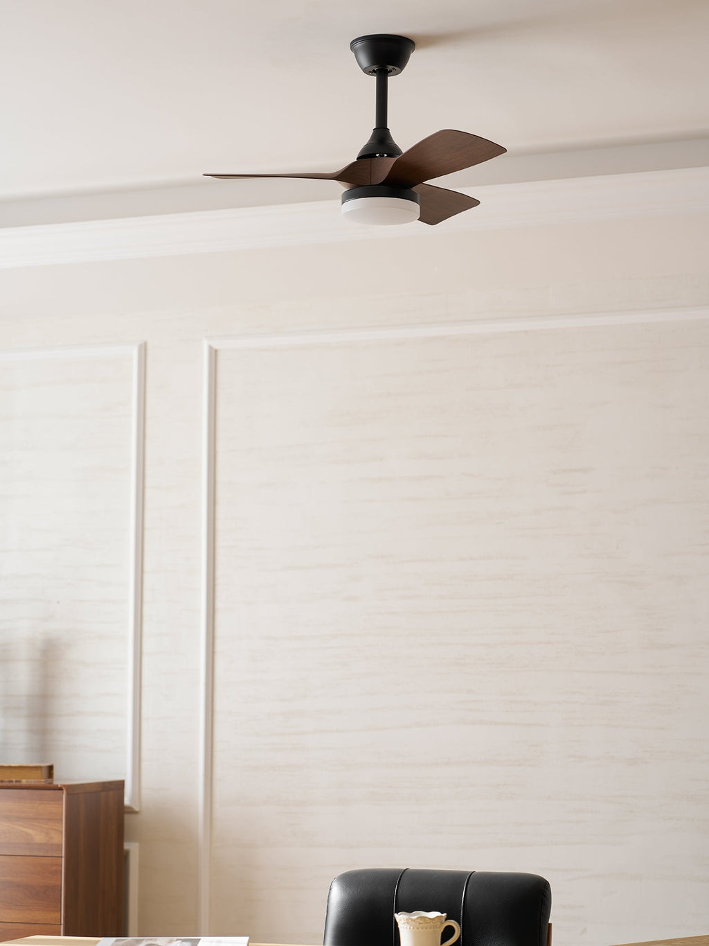 Close-framed view of this Clérachic fan with a lit light, above a panelled cream wall and a sideboard.