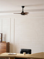 Wider view of this Clérachic ceiling fan above a light wood desk and a black leather chair, with a panelled cream wall behind.