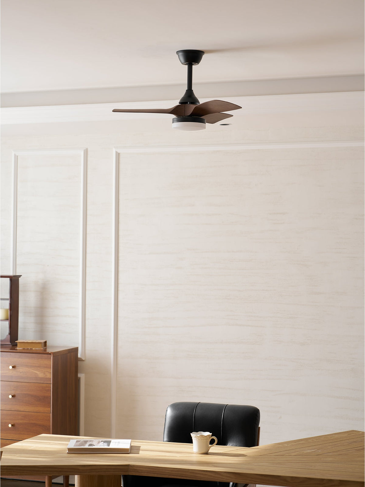 Wider view of this Clérachic ceiling fan above a light wood desk and a black leather chair, with a panelled cream wall behind.