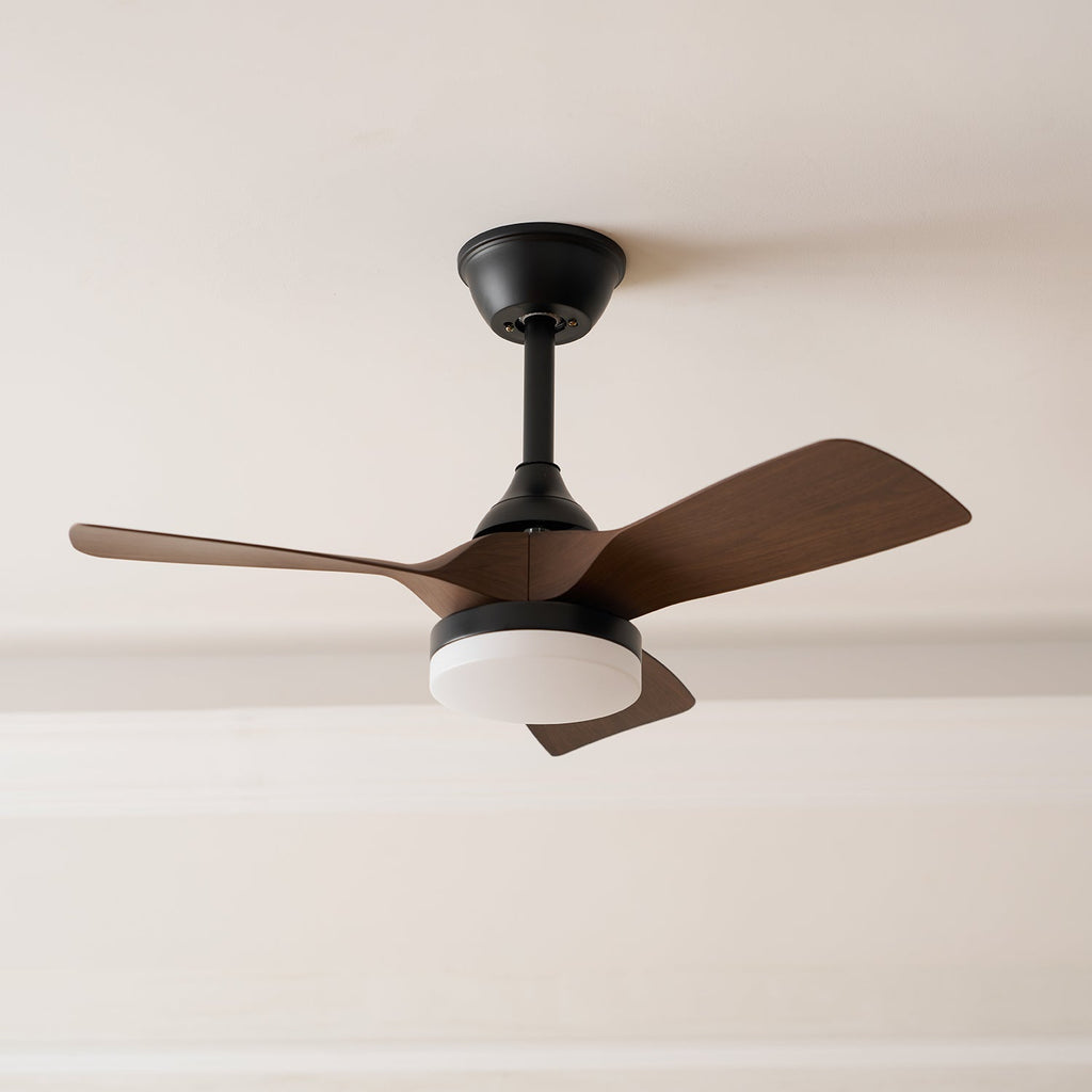 Angled view of this Clérachic ceiling fan, showing the black canopy, three walnut-grain blades and a lit light under a pale ceiling.