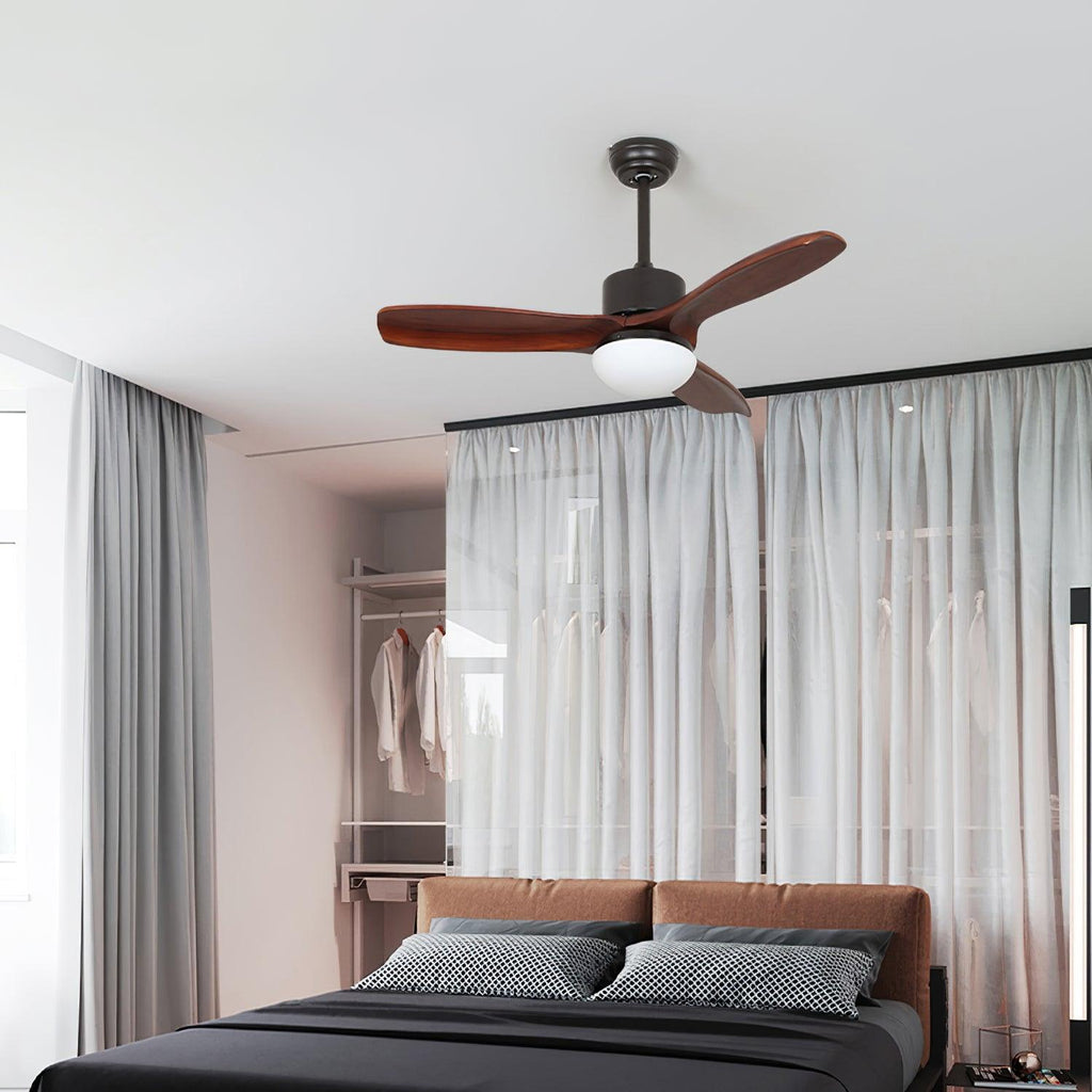 Black and dark brown ceiling fan from Clérachic with a round light, above a bed with grey linen and sheer curtains beside a wardrobe.