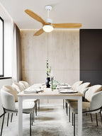 Light wooden-bladed ceiling fan from Clérachic above a dining table with cream chairs, in a room with a pale panelled wall.