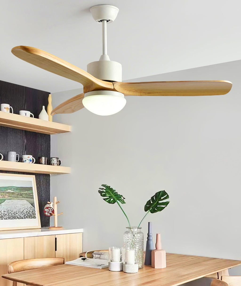 Lit ceiling fan from Clérachic with wooden blades above a wooden dining table, with open shelves and a monstera plant behind.