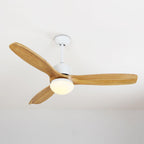 Ceiling fan from Clérachic with wooden blades and its round light switched on, below a pale ceiling.