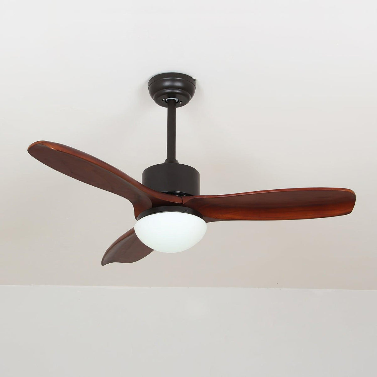 Black and dark brown ceiling fan with light from Clérachic, with deep red-brown blades and a lit frosted shade under a pale ceiling.