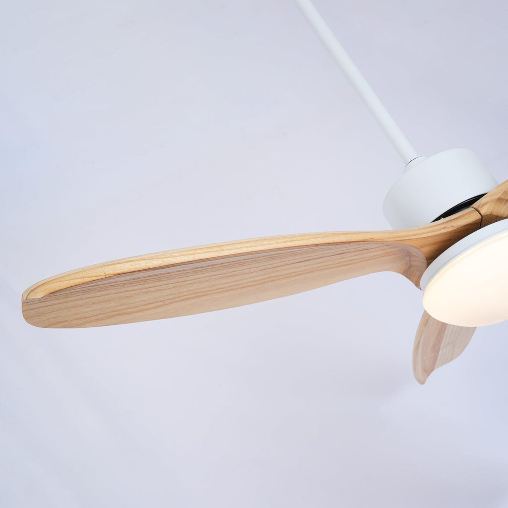 Angled view of a wooden blade and the white motor of this Clérachic ceiling fan, with the light shade glowing warm.