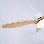 Angled view of a wooden blade and the white motor of this Clérachic ceiling fan, with the light shade glowing warm.