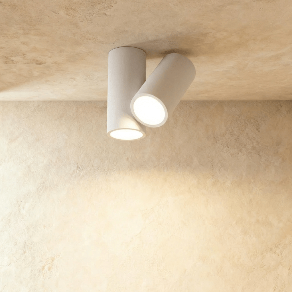 Clérachic white cylindrical ceiling light with two tilted round heads glowing warm white on a plaster ceiling