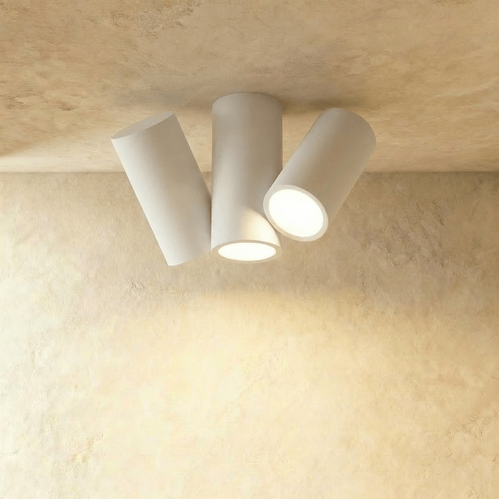 Clérachic white three-head cylindrical ceiling light with tilted round heads, lit warm white on plaster