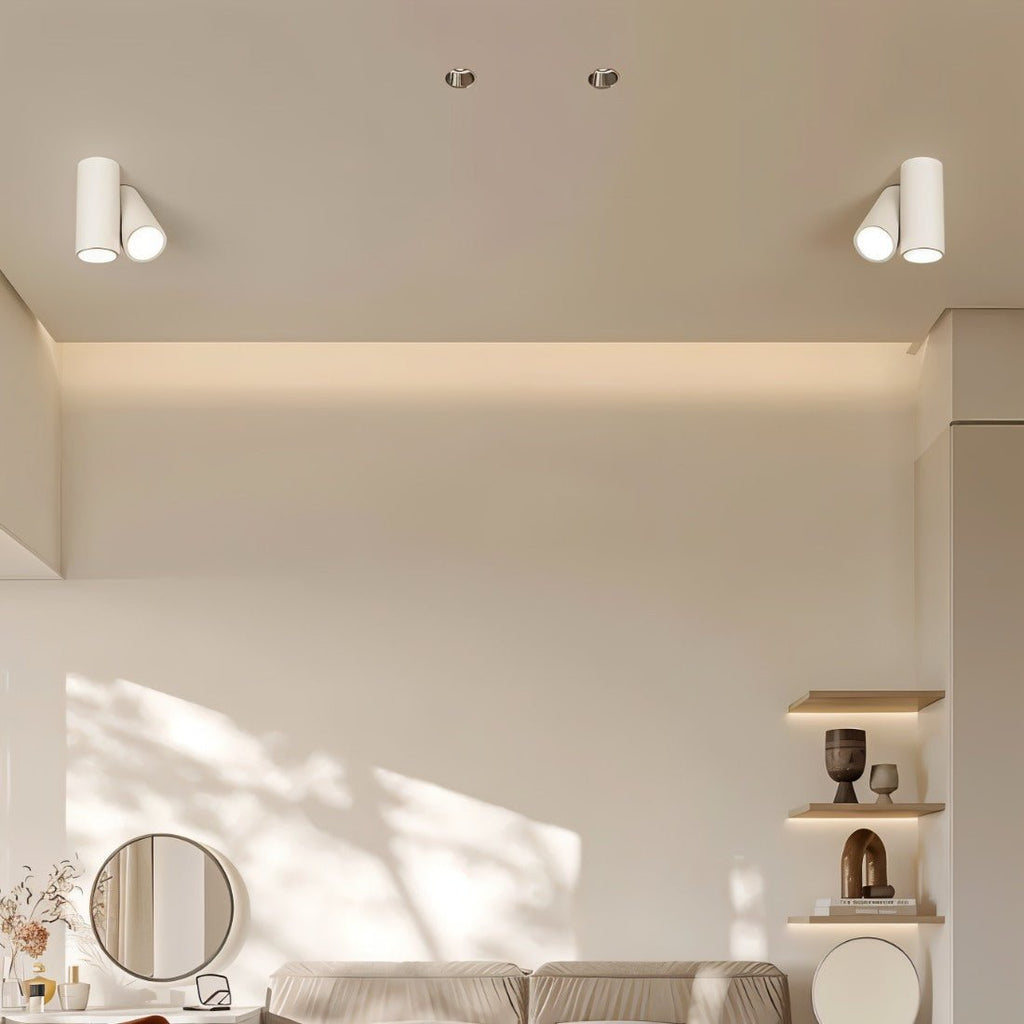 Pair of Clérachic white cylindrical two-head ceiling lights above a living room with shelves and a round mirror