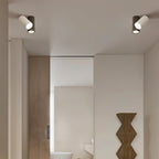Pair of Clérachic ceiling lights, each a white and a dark cylinder, in a hallway beside a wooden door