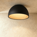Clérachic larger black domed ceiling light with a wood-grain interior glowing warmly, fixed flush to a limewashed ceiling.