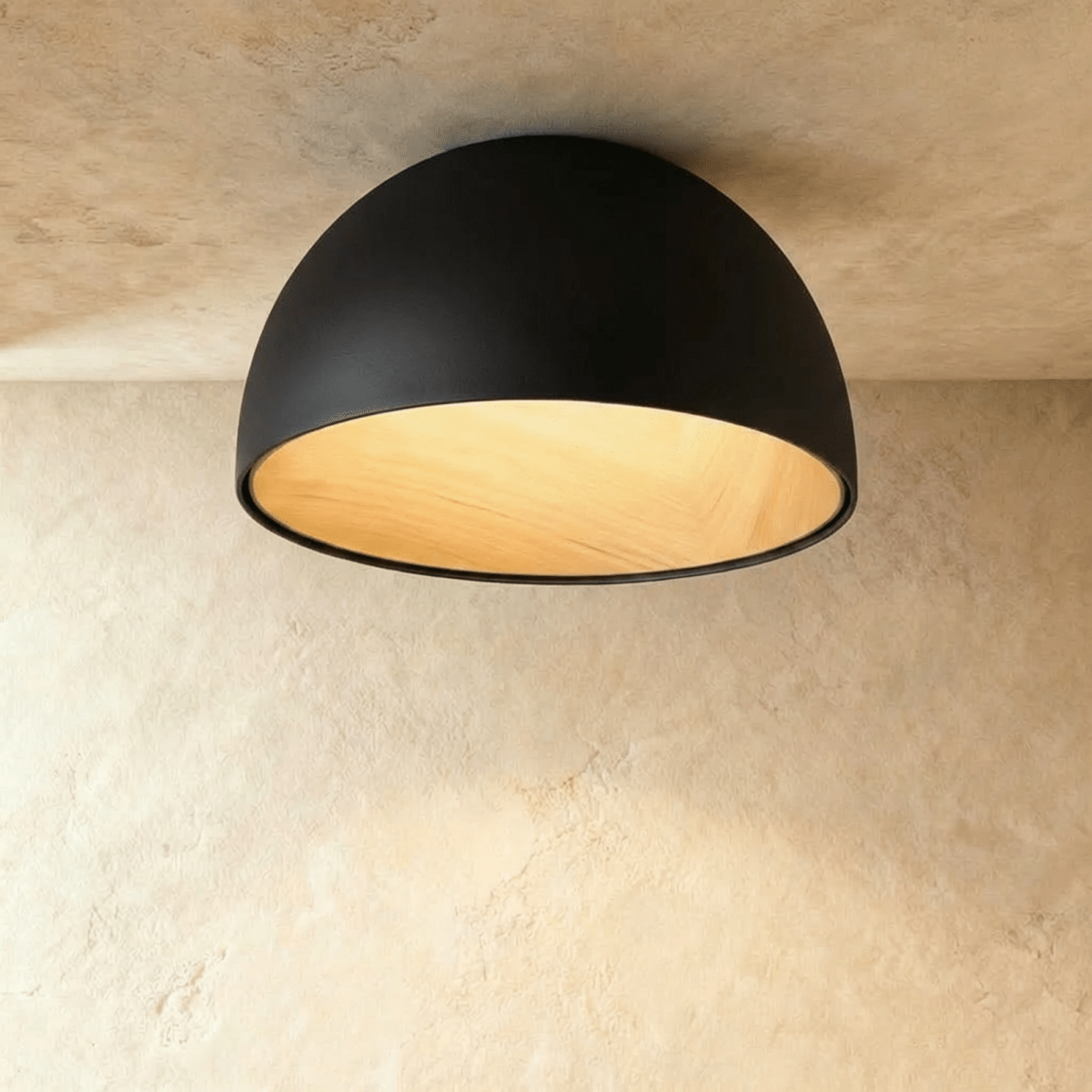 Clérachic larger black domed ceiling light with a wood-grain interior glowing warmly, fixed flush to a limewashed ceiling.