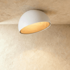 Clérachic white ceiling light with an angled, slanted-cut dome and a glowing wood-grain interior on a limewashed ceiling.