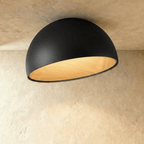 Clérachic larger black angled-dome ceiling light with a wide, glowing wood-grain interior on a limewashed ceiling.