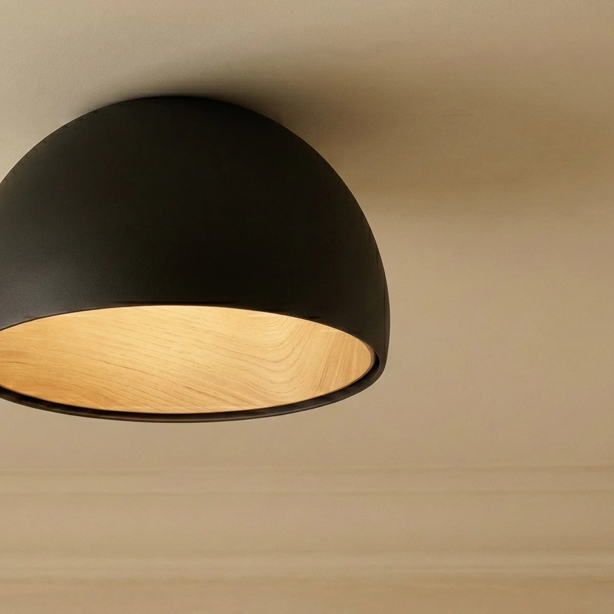 Close view of the Clérachic black dome ceiling light, its matt shell and oak-grain interior glowing warmly overhead.