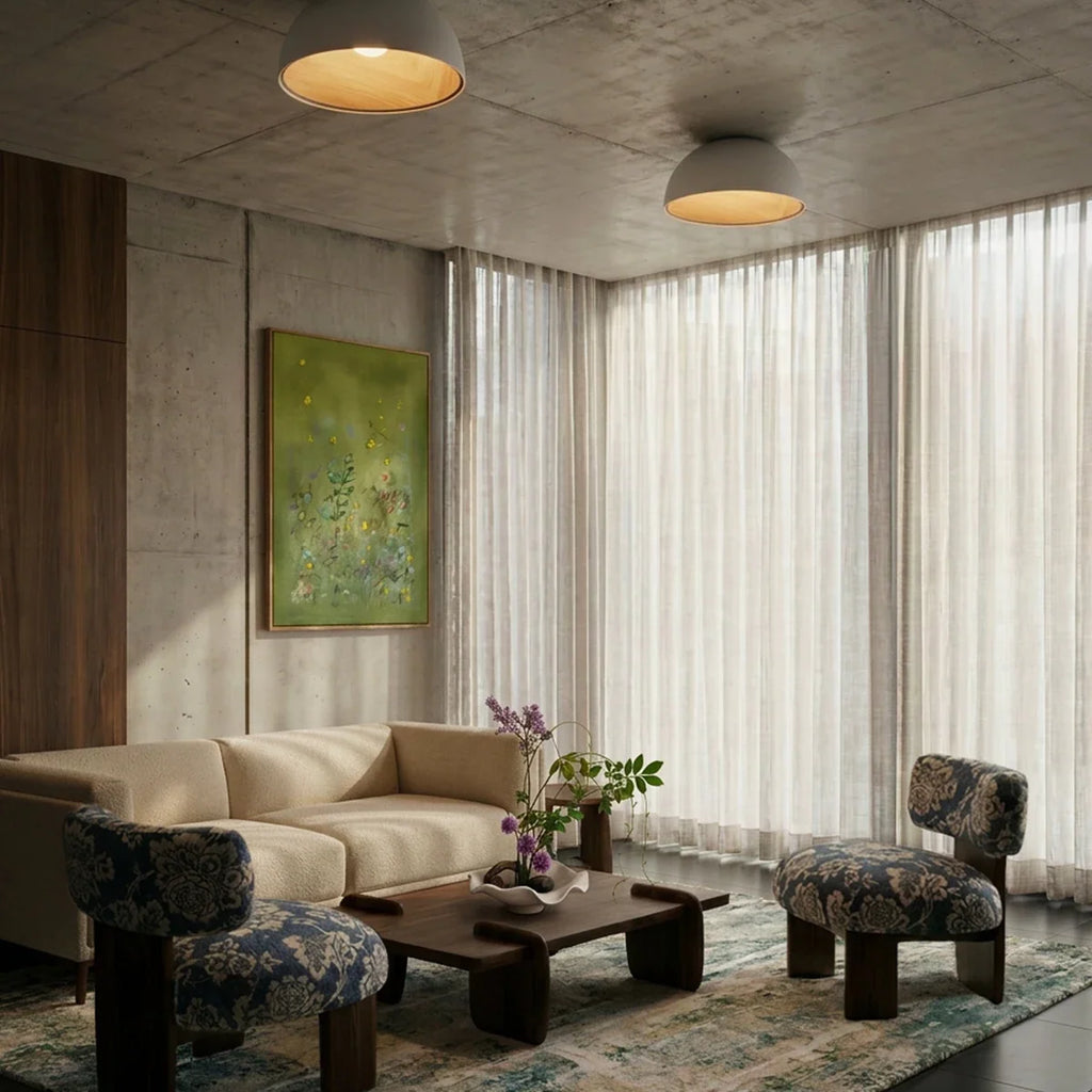 Two Clérachic white domed ceiling lights on a concrete ceiling above a cream sofa, patterned chairs and sheer curtains.