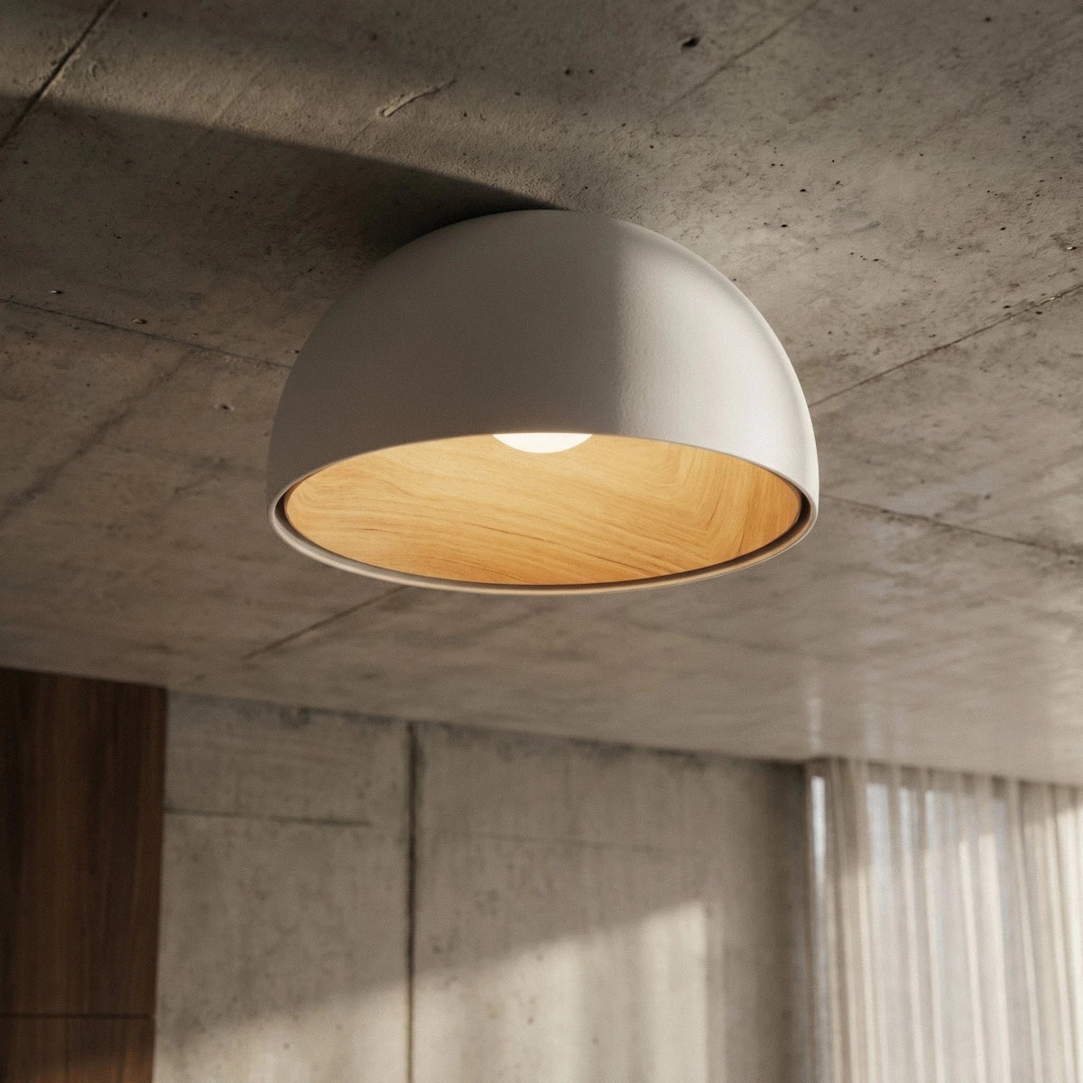 Clérachic white domed ceiling light on a raw concrete ceiling, its wood-grain interior lit, beside sheer curtains and a walnut panel.