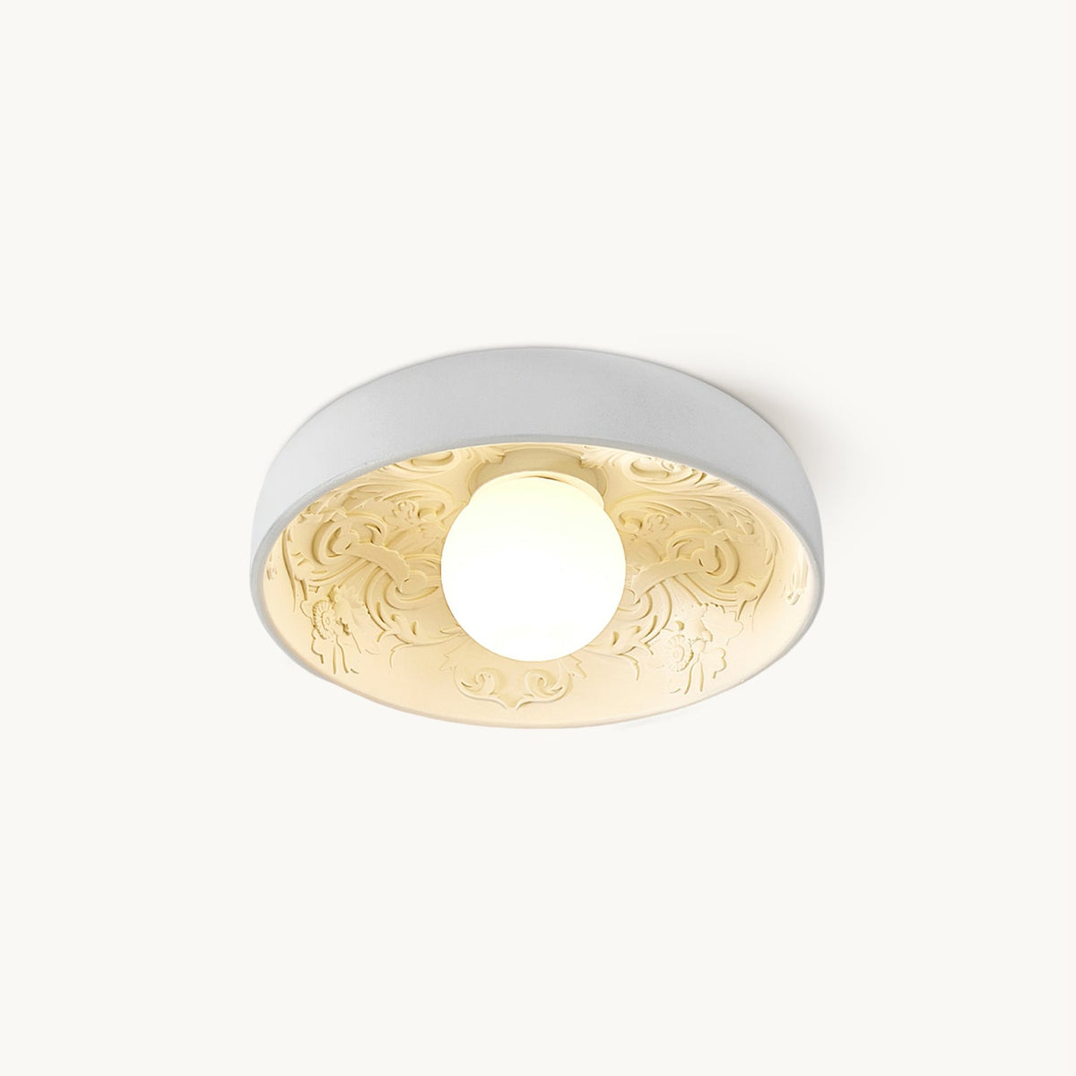 Clérachic white flush-mount ceiling light with a carved floral relief inside the bowl and a lit round globe, on a plain white backdrop.