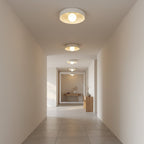 Row of Clérachic white bowl ceiling lights running down a long, pale hallway with a wooden console at the far end.