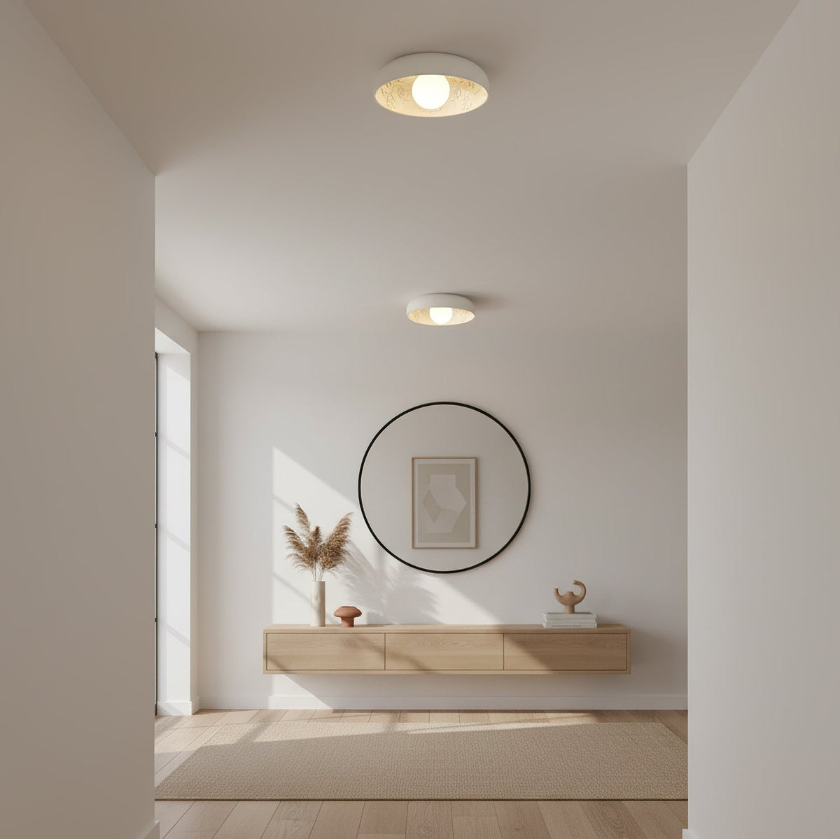 Two Clérachic carved-resin ceiling lights lit in a pale room, above a round black mirror and a floating wooden shelf with dried grasses.