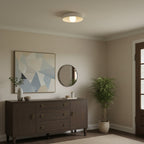 A Clérachic white bowl light on a beige ceiling, above a dark wood sideboard, a green plant and abstract art in a calm room.