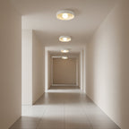 Clérachic flush-mount lights receding along a tiled corridor, each lit with a round globe inside a white bowl.