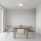 Clérachic white bowl light overhead in a minimal room with a light wood dining table and four grey chairs.