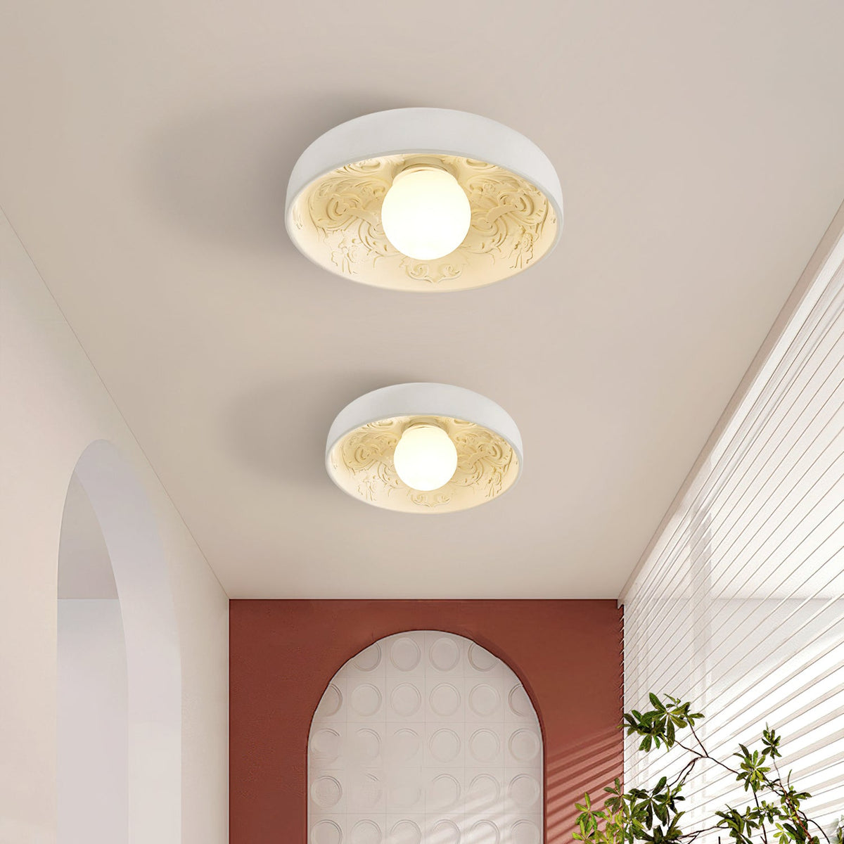 Two Clérachic white bowl lights lit on a hallway ceiling, near an arched opening and a terracotta-coloured wall.