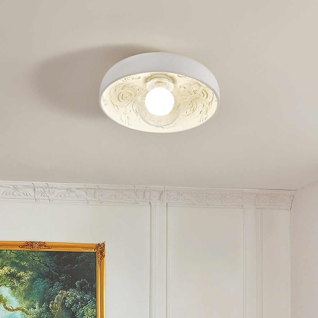 Lit Clérachic bowl light with an engraved leaf pattern inside, on a beige ceiling above panelled white walls and a gilt frame.