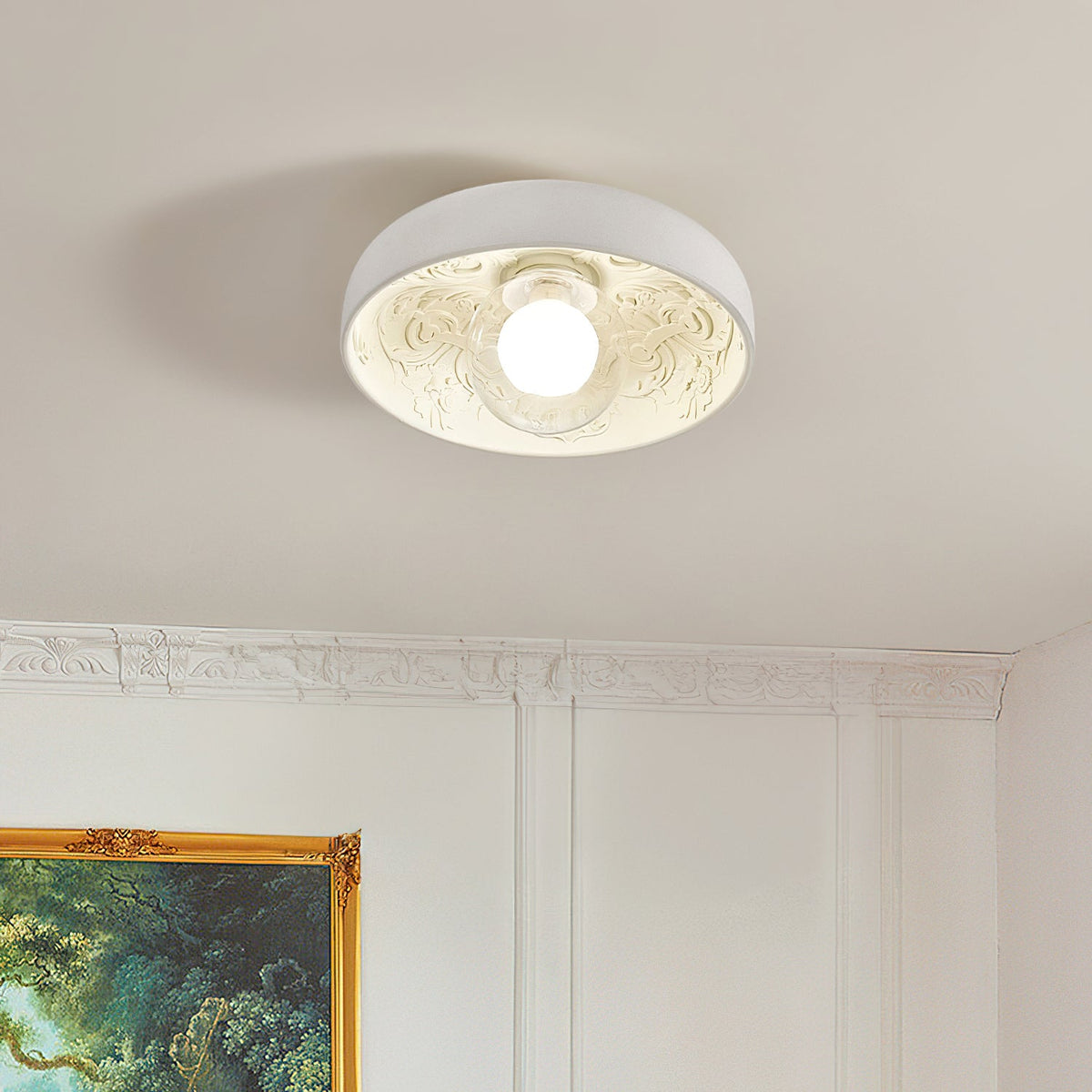 Lit Clérachic bowl light with an engraved leaf pattern inside, on a beige ceiling above panelled white walls and a gilt frame.