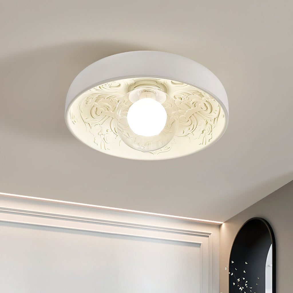 Close view of the Clérachic bowl light's carved scrollwork and glowing globe, with a cove light line along the wall behind.