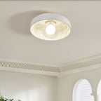 Clérachic ceiling light lit under a ribbed cornice, its carved white interior glowing around the round globe.