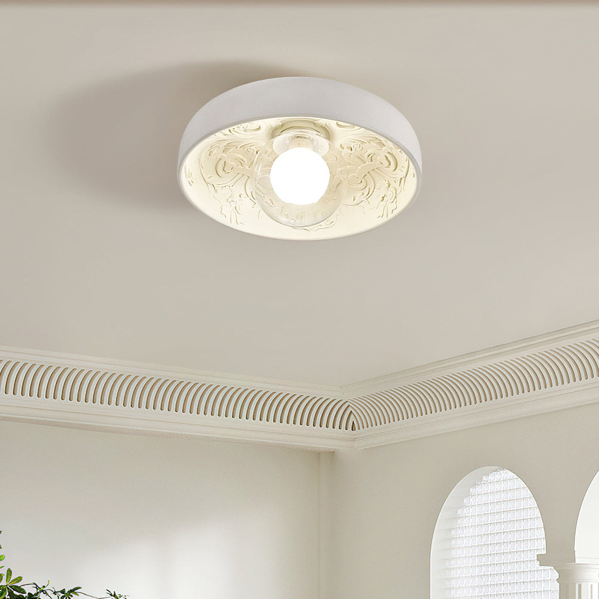 Clérachic ceiling light lit under a ribbed cornice, its carved white interior glowing around the round globe.