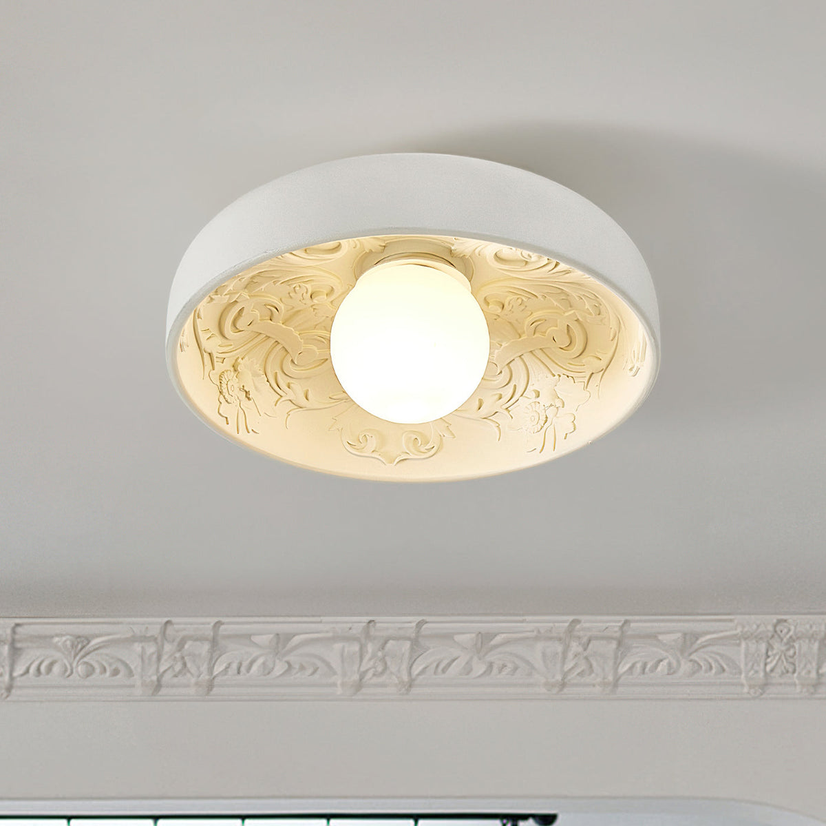 Clérachic white bowl light with carved floral scrolls inside and a frosted globe, shown under a decorative cornice.