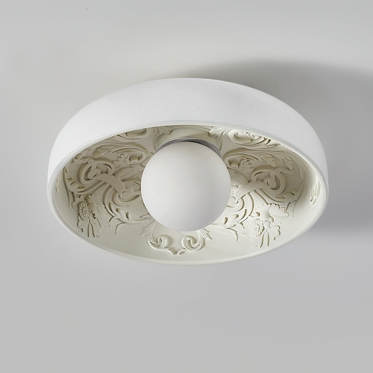 Clérachic flush light seen from below, the clear glass globe unlit, with detailed ornamental relief lining the white bowl.
