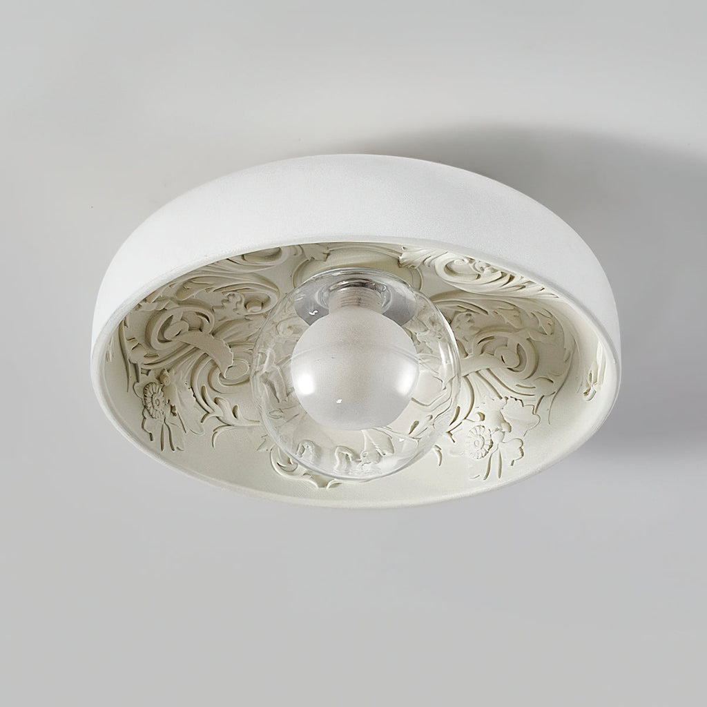 This Clérachic ceiling light with a clear glass globe, switched off, shows its carved floral pattern on a pale grey ceiling.