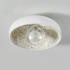 This Clérachic ceiling light with a clear glass globe, switched off, shows its carved floral pattern on a pale grey ceiling.